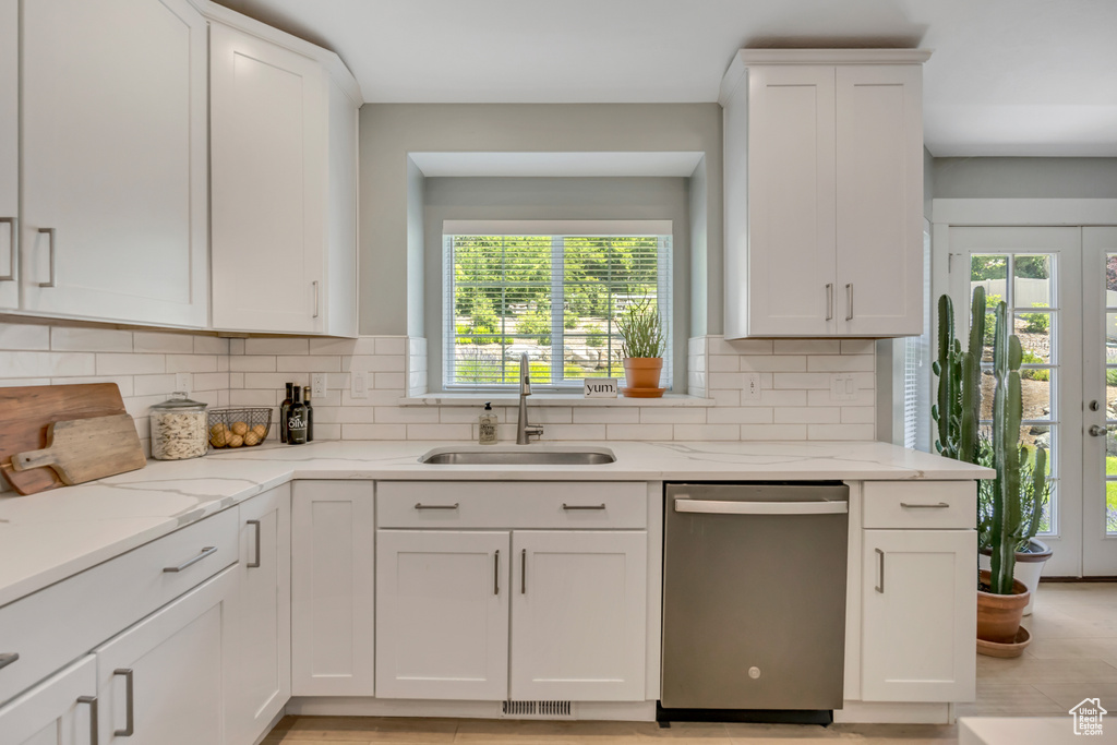 Kitchen with stainless steel dishwasher, white cabinets, decorative backsplash, and light stone counters