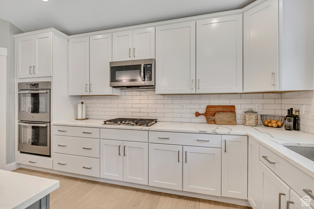 Kitchen featuring stainless steel appliances, white cabinetry, tasteful backsplash, and light wood-style flooring