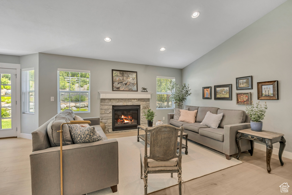 Living room featuring healthy amount of natural light, light wood finished floors, a stone fireplace, recessed lighting, and vaulted ceiling