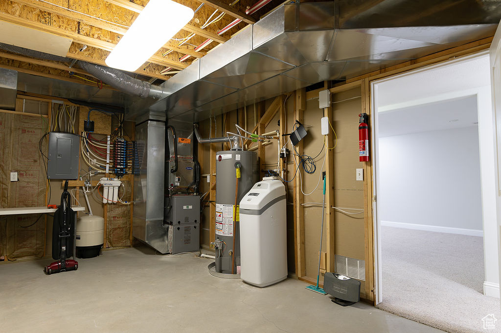 Unfinished basement featuring heating unit, electric panel, a water softener system, and gas water heater