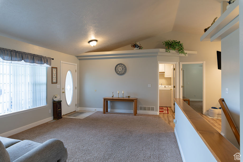 Entrance foyer featuring washer / dryer, light carpet, and lofted ceiling