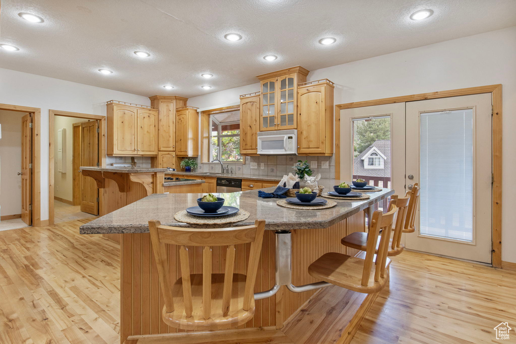Kitchen with white microwave, a breakfast bar, stainless steel dishwasher, light wood finished floors, and glass insert cabinets