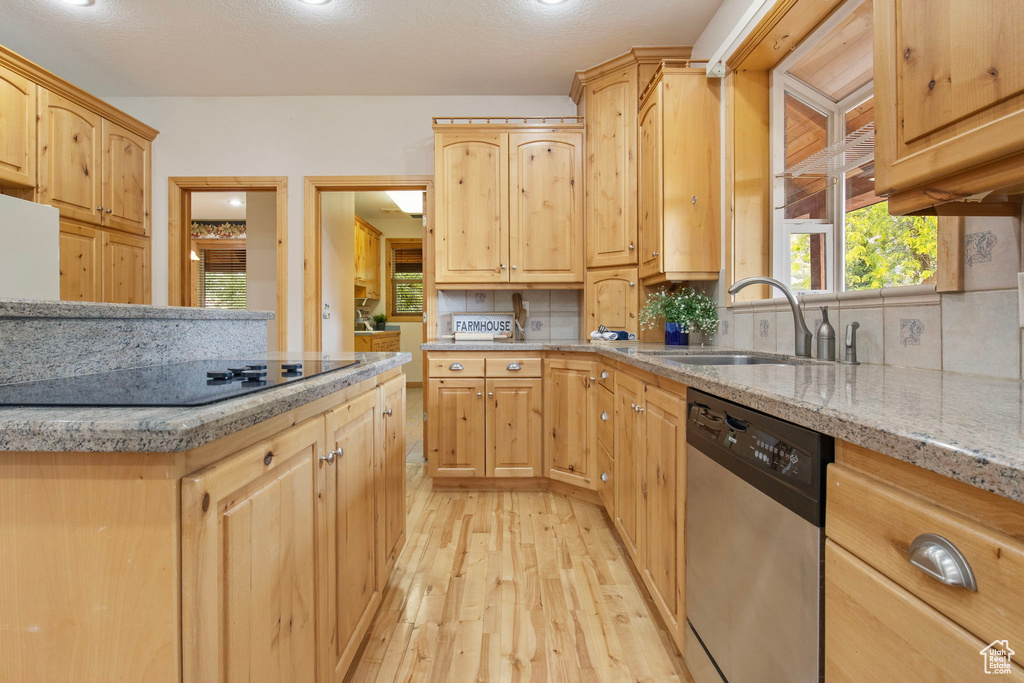 Kitchen with stainless steel dishwasher, black electric cooktop, light brown cabinets, and light wood-style flooring
