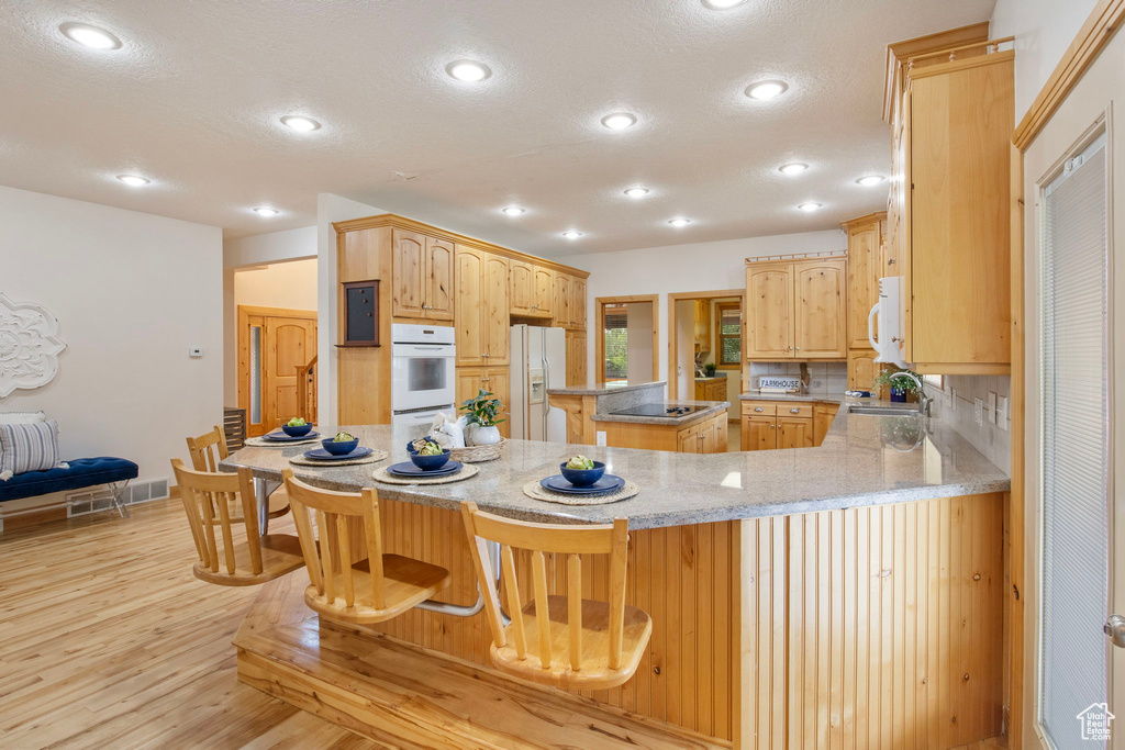 Kitchen with white appliances, a textured ceiling, light wood-style flooring, a kitchen island, and a peninsula