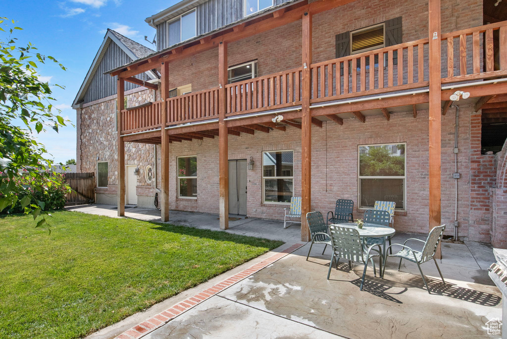 Back of property with brick siding, a patio, board and batten siding, and a balcony