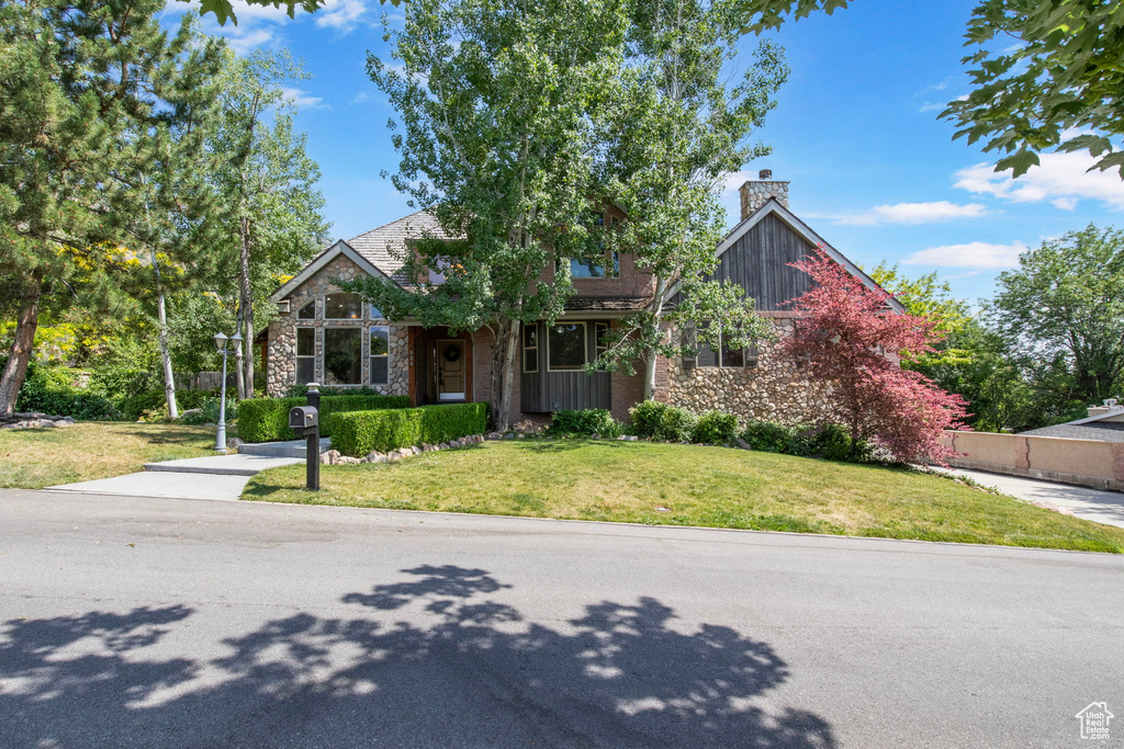 View of front of home with a chimney, stone siding, and a front yard