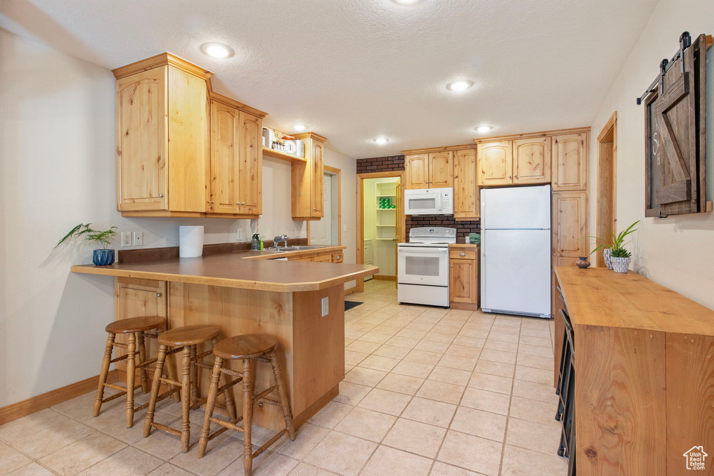 Kitchen with white appliances, a peninsula, light tile patterned floors, a kitchen breakfast bar, and a barn door