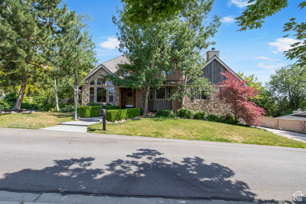 View of front of home with a chimney, a front lawn, and stone siding