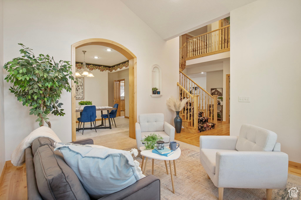 Living room with arched walkways, high vaulted ceiling, stairs, a chandelier, and light wood-style flooring