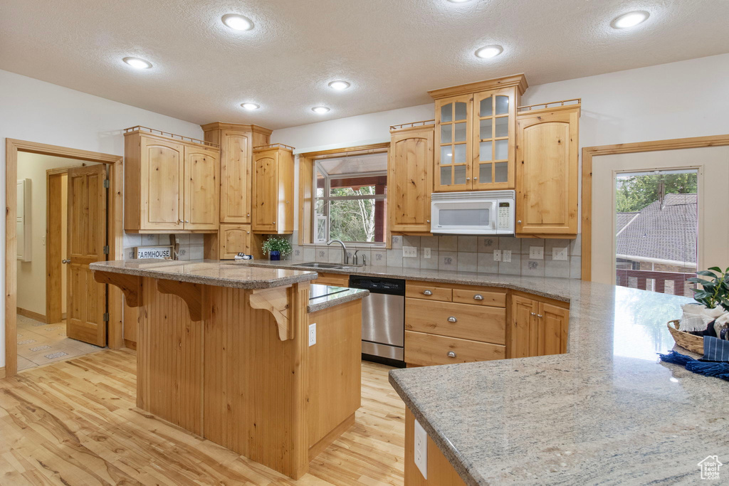 Kitchen featuring white microwave, dishwasher, a kitchen breakfast bar, light wood-style floors, and glass insert cabinets