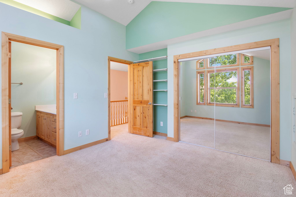 Unfurnished bedroom with a closet, carpet flooring, ensuite bathroom, and high vaulted ceiling