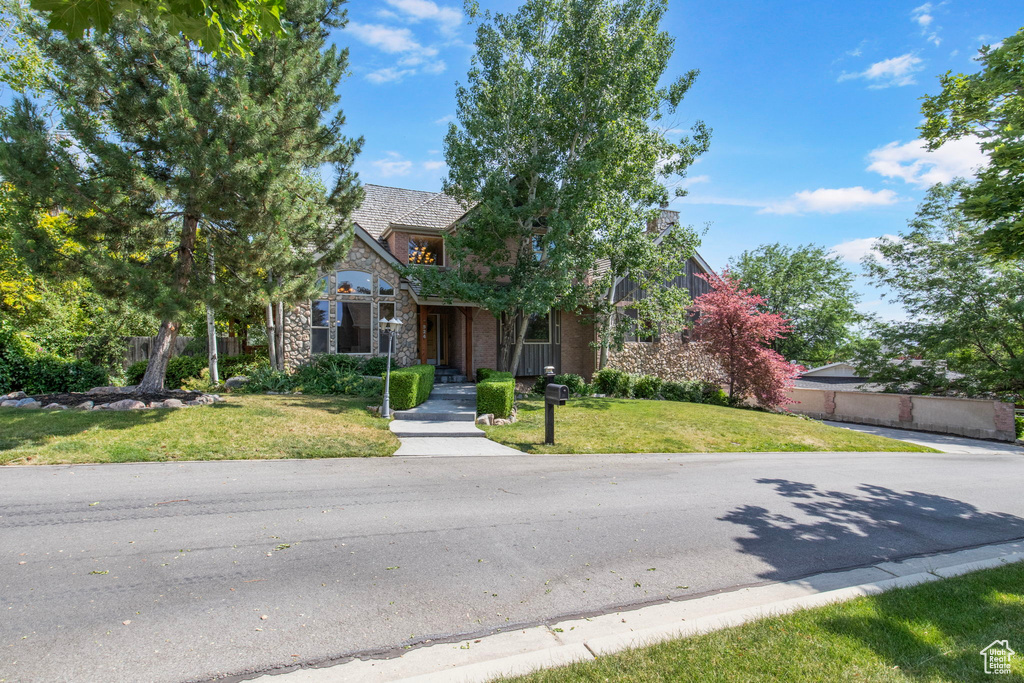 View of property hidden behind natural elements with stone siding and a front yard