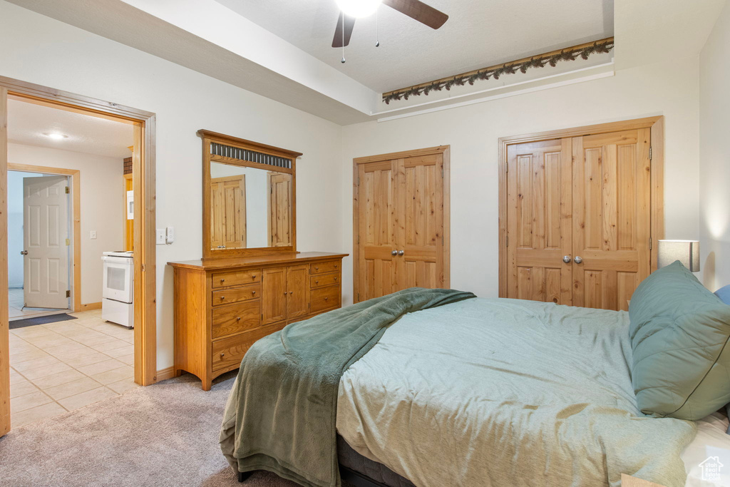 Bedroom featuring light tile patterned floors, light carpet, a ceiling fan, and connected bathroom