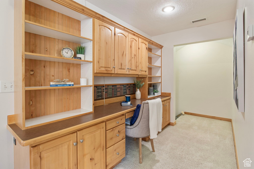 Home office featuring built in desk, light colored carpet, and a textured ceiling