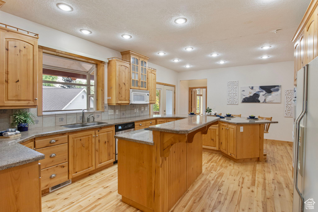 Kitchen with white appliances, a peninsula, a breakfast bar, light wood finished floors, and a kitchen island