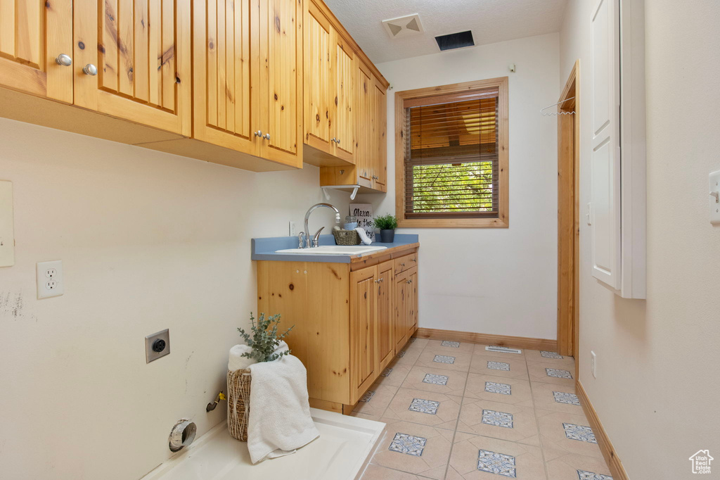 Laundry area with hookup for an electric dryer, cabinet space, and light tile patterned floors