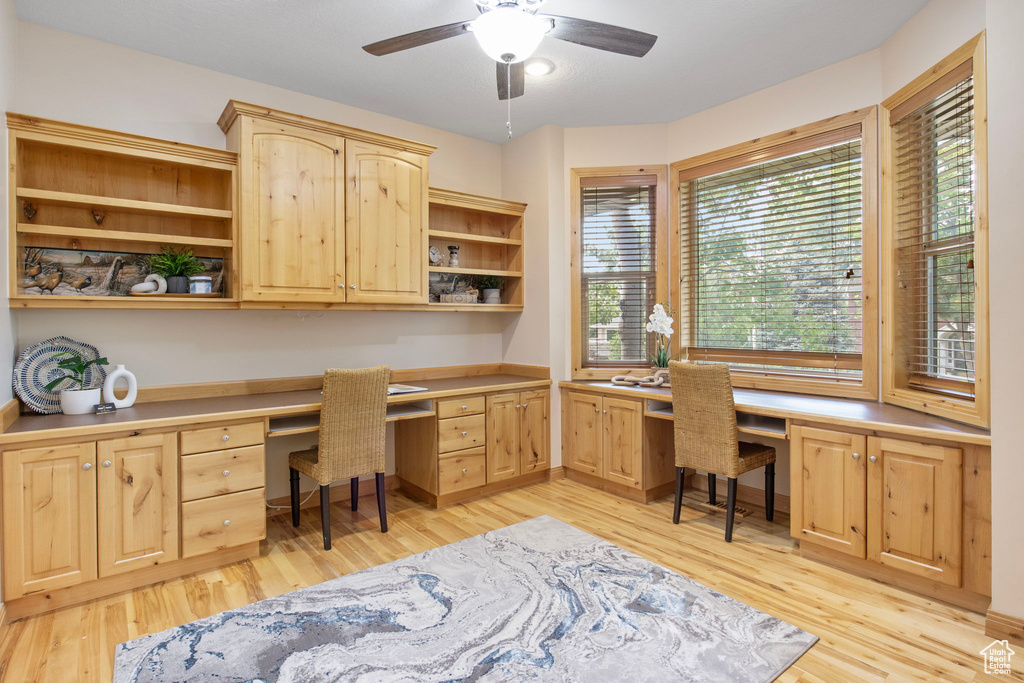 Office with built in study area, light wood finished floors, and ceiling fan