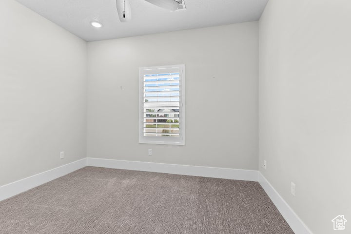 Carpeted empty room featuring a ceiling fan and baseboards