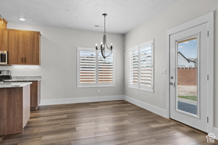 Unfurnished dining area with healthy amount of natural light, a textured ceiling, a chandelier, and wood finished floors