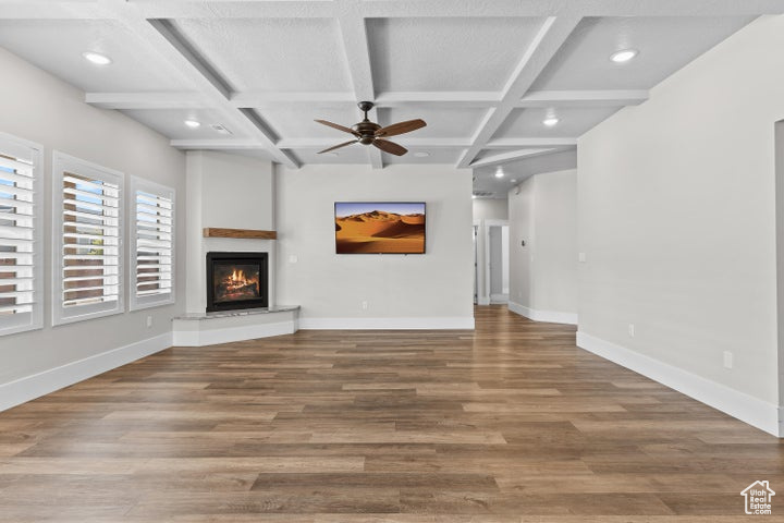 Unfurnished living room with a glass covered fireplace, coffered ceiling, ceiling fan, wood finished floors, and recessed lighting