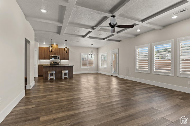 Unfurnished living room with dark wood-style floors, coffered ceiling, ceiling fan, beamed ceiling, and a chandelier