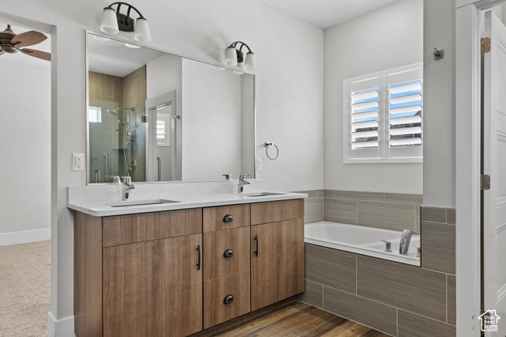 Full bathroom with double vanity, a shower stall, a bath, and a ceiling fan