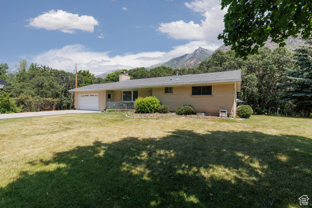 Ranch-style house featuring concrete driveway, a mountain view, an attached garage, a front yard, and brick siding