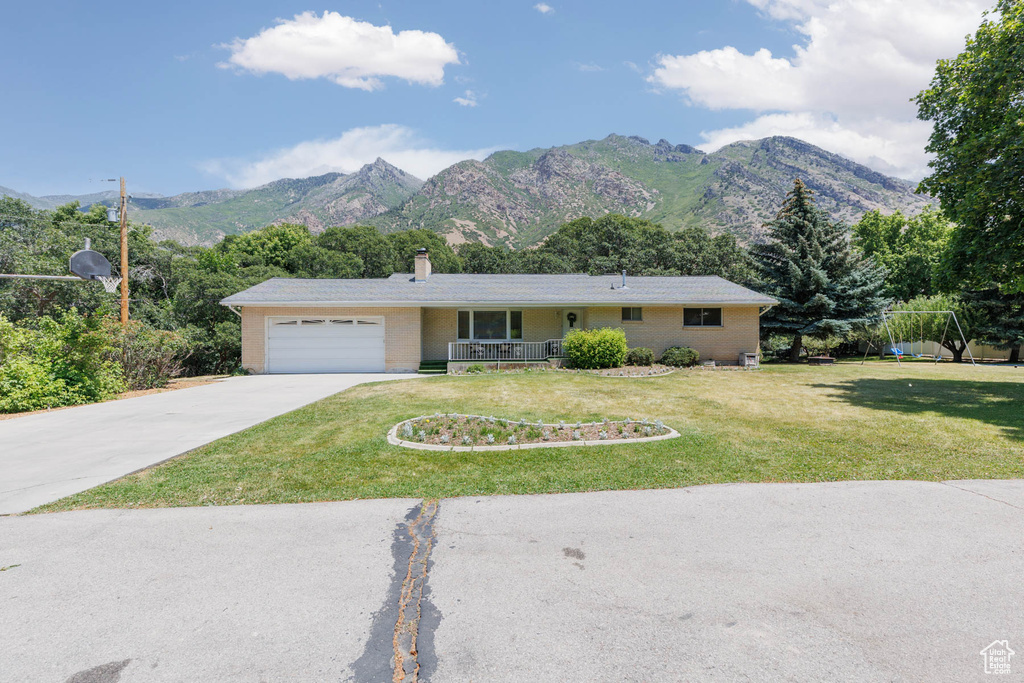 Ranch-style house with a garage, driveway, a mountain view, brick siding, and a front lawn