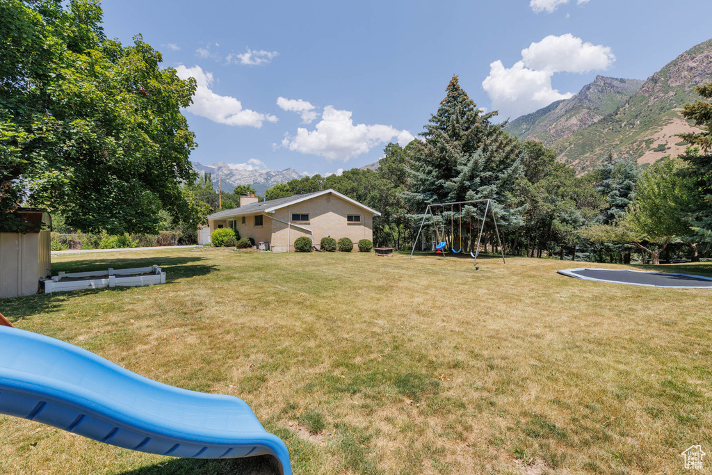 View of grassy yard with a playground and a mountain view