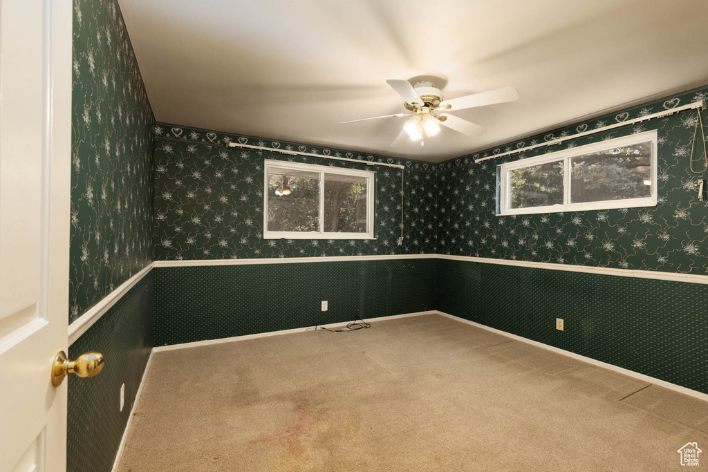 Carpeted empty room featuring wallpapered walls, ceiling fan, and wainscoting