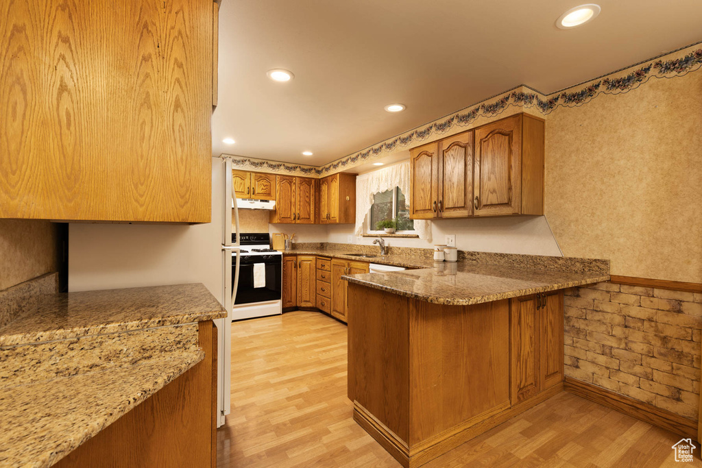 Kitchen with white range with electric cooktop, under cabinet range hood, brown cabinets, light wood finished floors, and recessed lighting