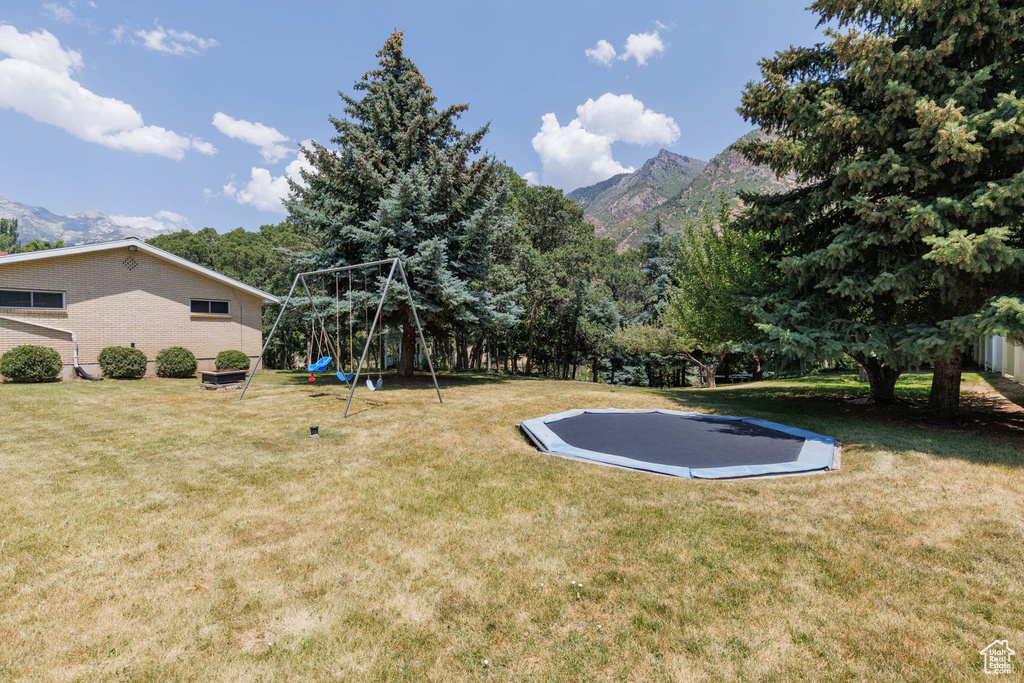 View of grassy yard with a playground, a mountain view, and a trampoline