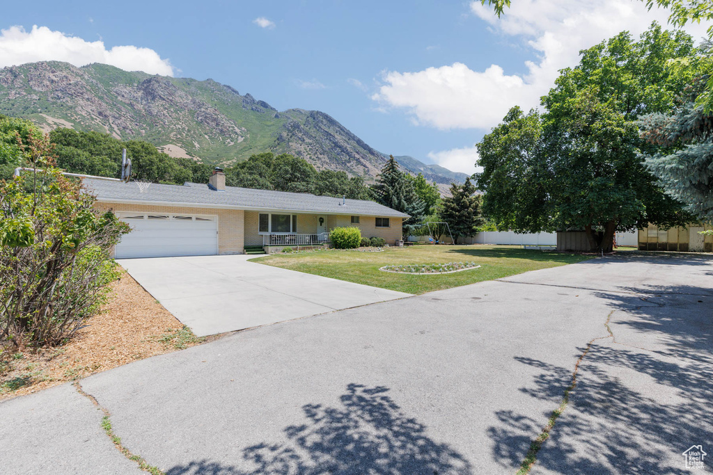 Ranch-style house featuring a chimney, driveway, a garage, a mountain view, and a front lawn
