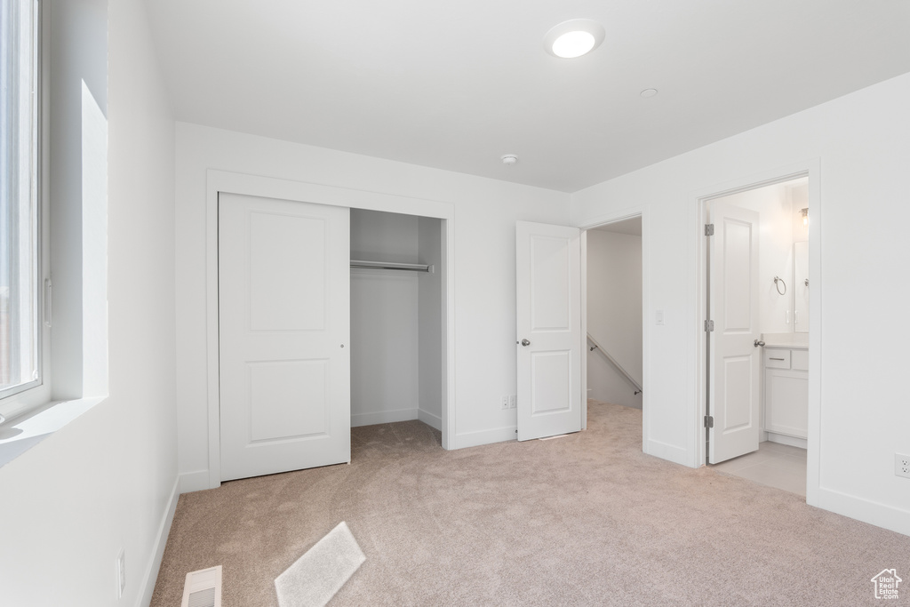 Unfurnished bedroom featuring light colored carpet, a closet, and ensuite bath