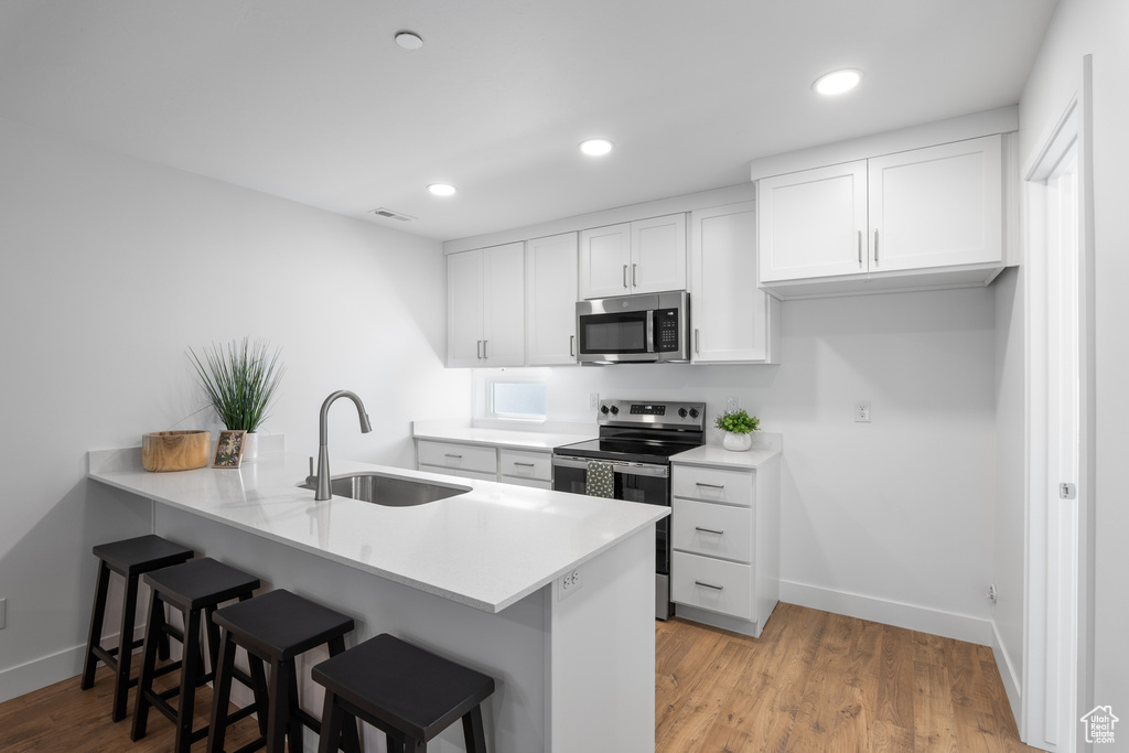 Kitchen featuring appliances with stainless steel finishes, a kitchen bar, a peninsula, white cabinetry, and recessed lighting
