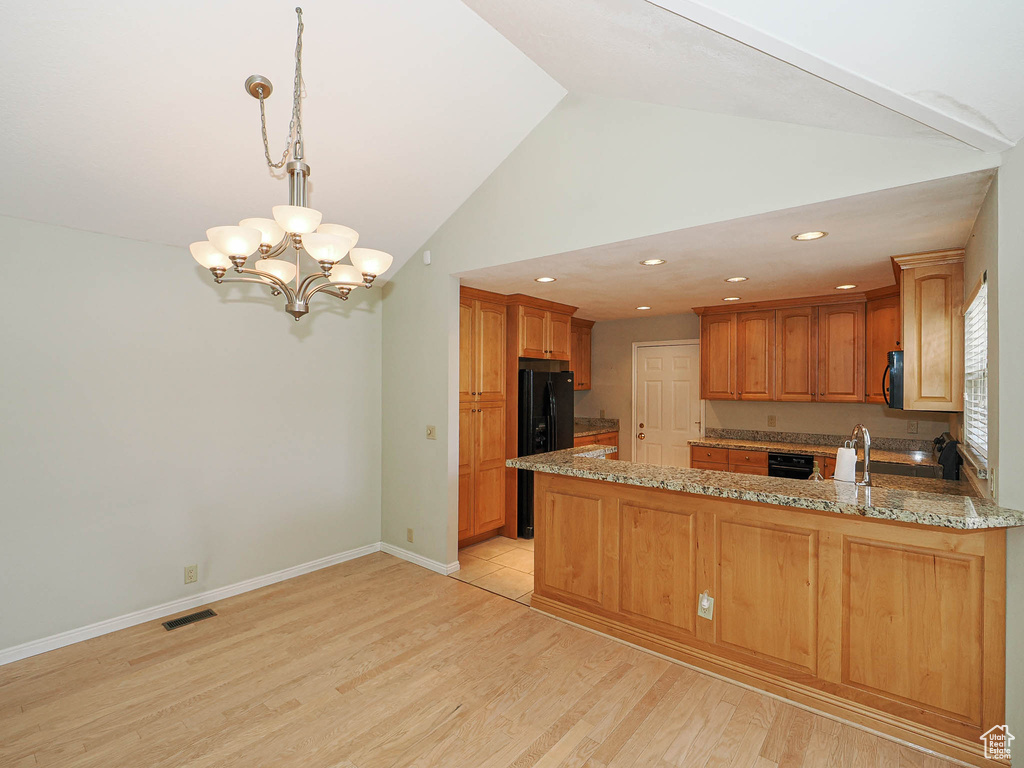 Kitchen with a peninsula, a chandelier, light wood-style flooring, light stone counters, and lofted ceiling