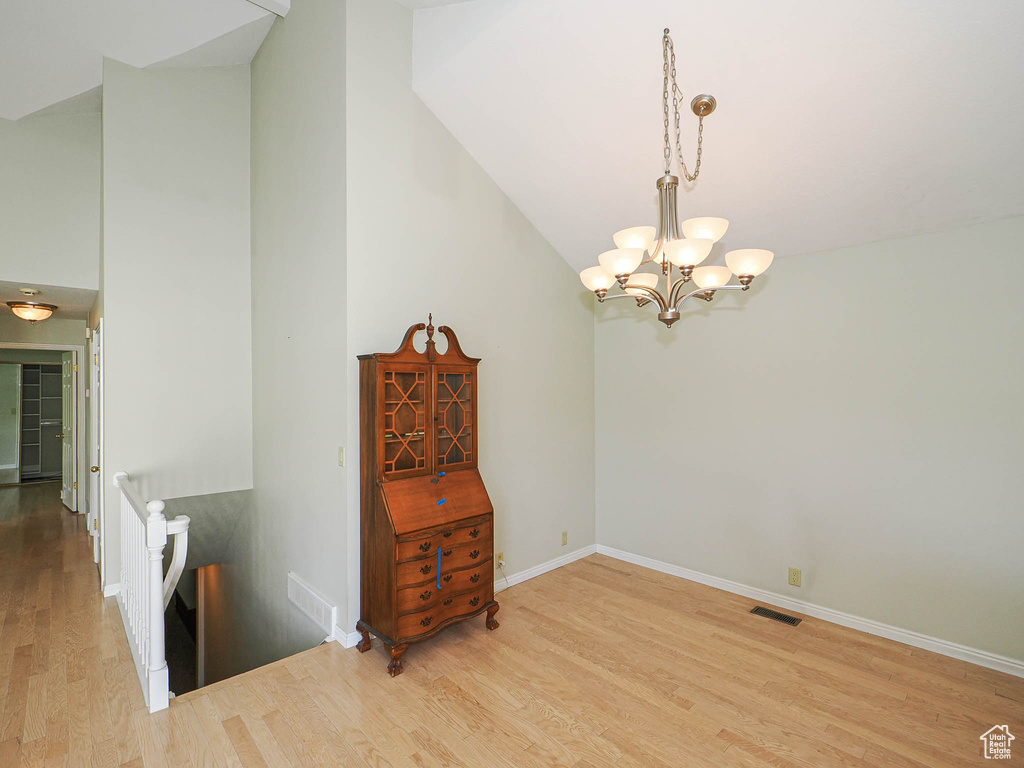 Spare room with a chandelier, wood finished floors, and lofted ceiling