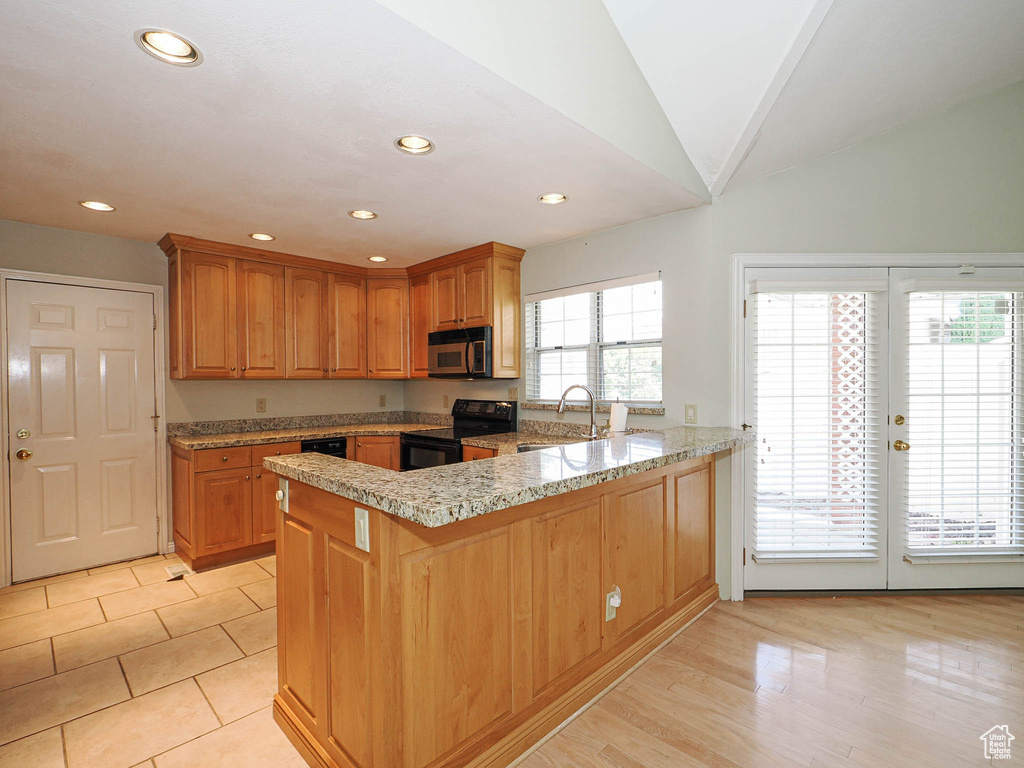 Kitchen with electric range, stainless steel microwave, a peninsula, recessed lighting, and light stone countertops