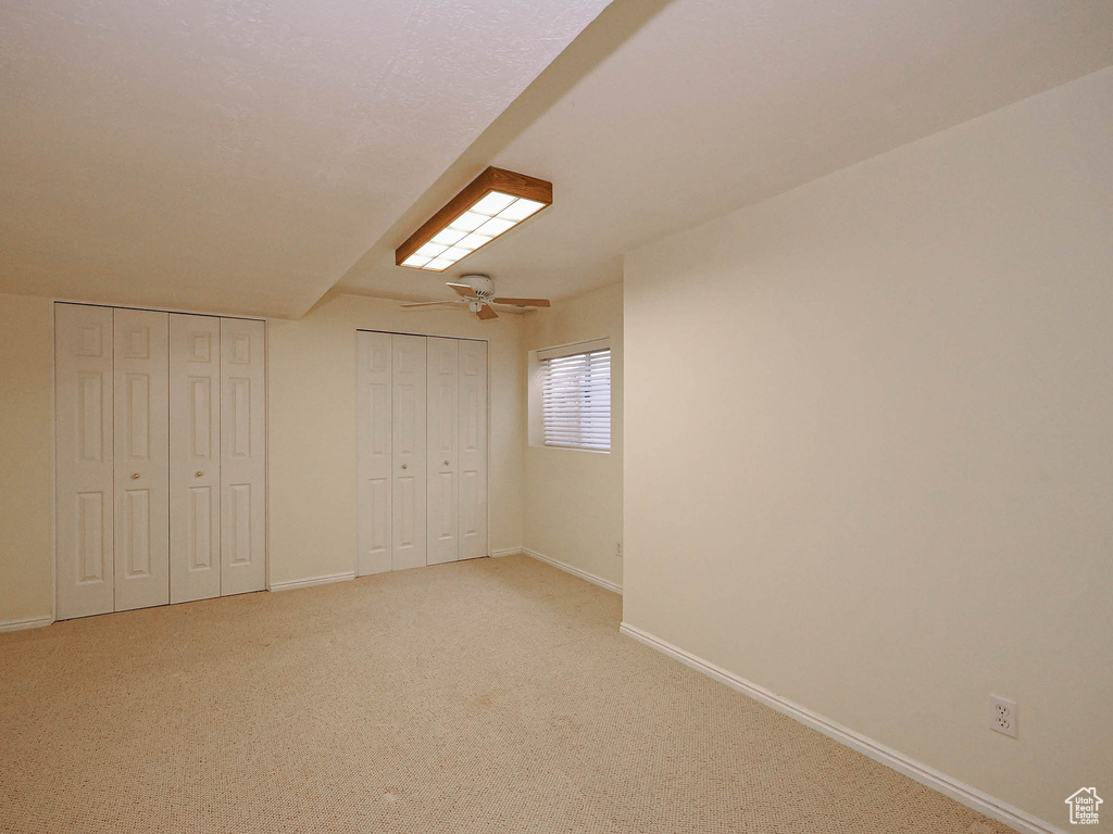 Unfurnished bedroom featuring a ceiling fan, light colored carpet, and two closets