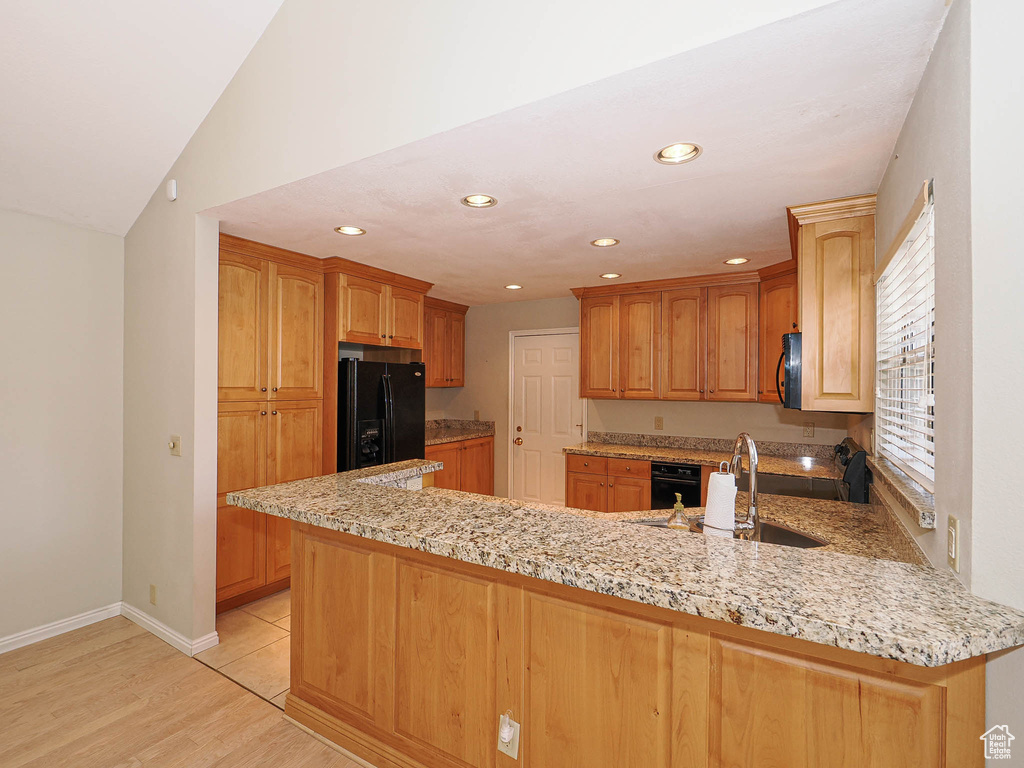 Kitchen featuring black appliances, a peninsula, light stone counters, recessed lighting, and light wood-style flooring