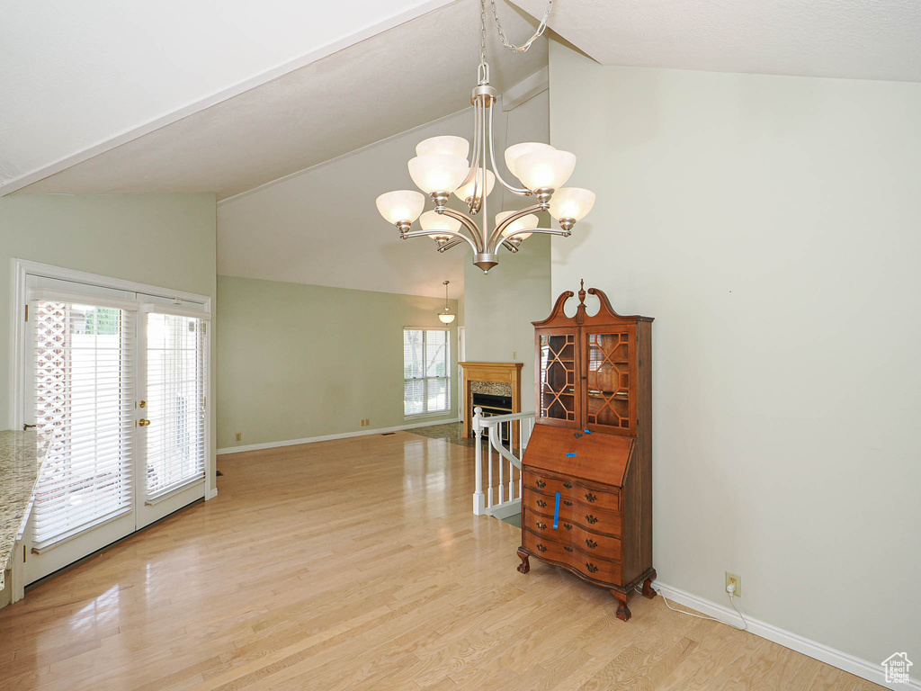 Living room featuring high vaulted ceiling, light wood-style floors, a chandelier, and a fireplace