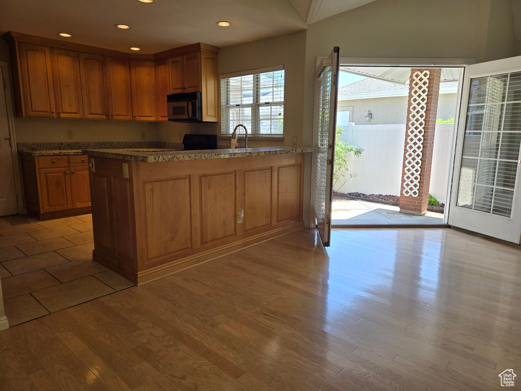 Kitchen featuring a peninsula, light wood-style floors, recessed lighting, brown cabinets, and dark stone counters