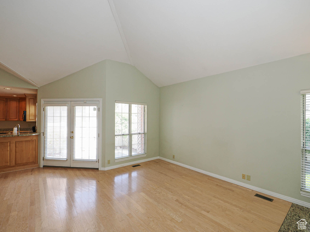 Unfurnished living room featuring light wood-type flooring and vaulted ceiling