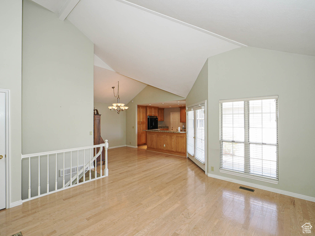 Unfurnished living room featuring a chandelier, light wood-type flooring, and high vaulted ceiling