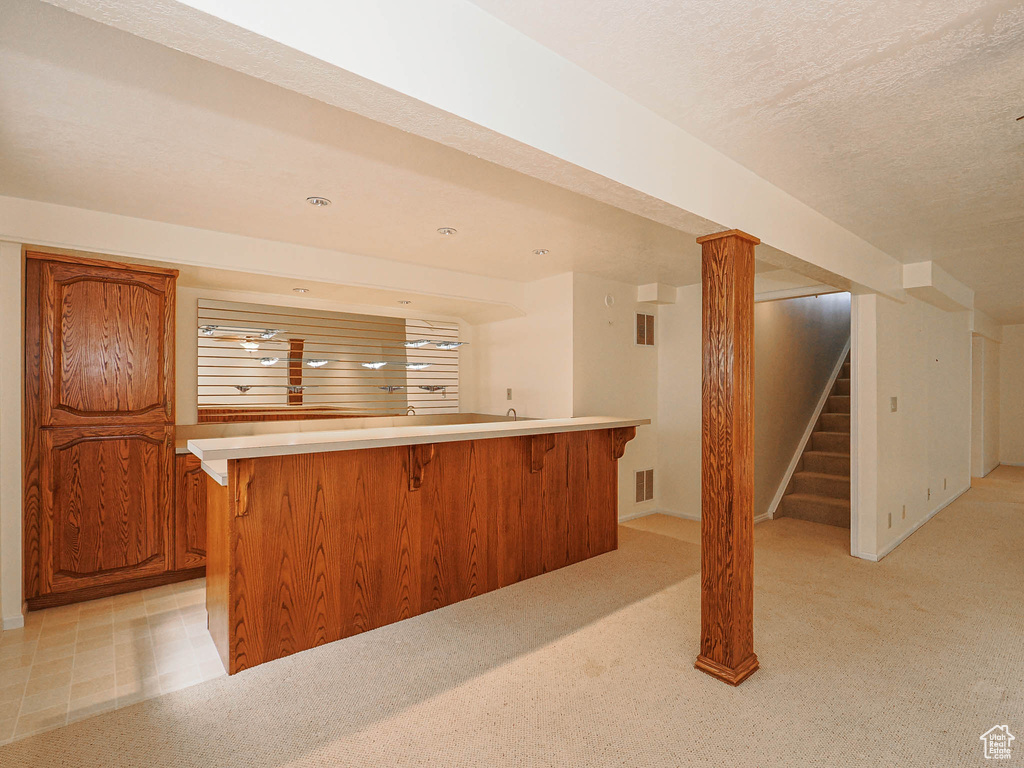 Indoor wet bar with stairway, light colored carpet, and a textured ceiling