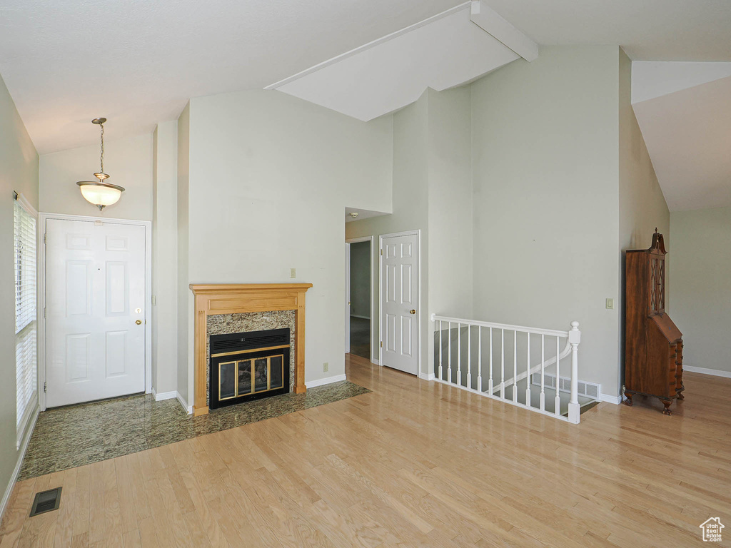 Unfurnished living room with high vaulted ceiling, light wood-type flooring, beam ceiling, and a fireplace