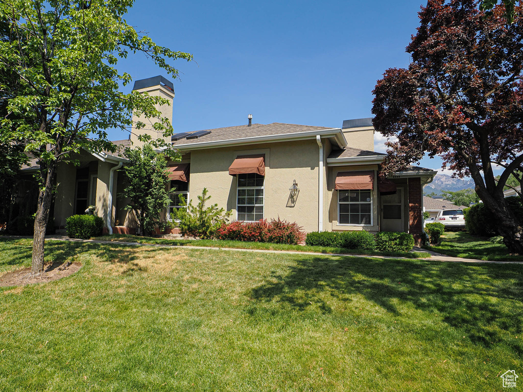 View of front of property with a chimney, stucco siding, and a front yard