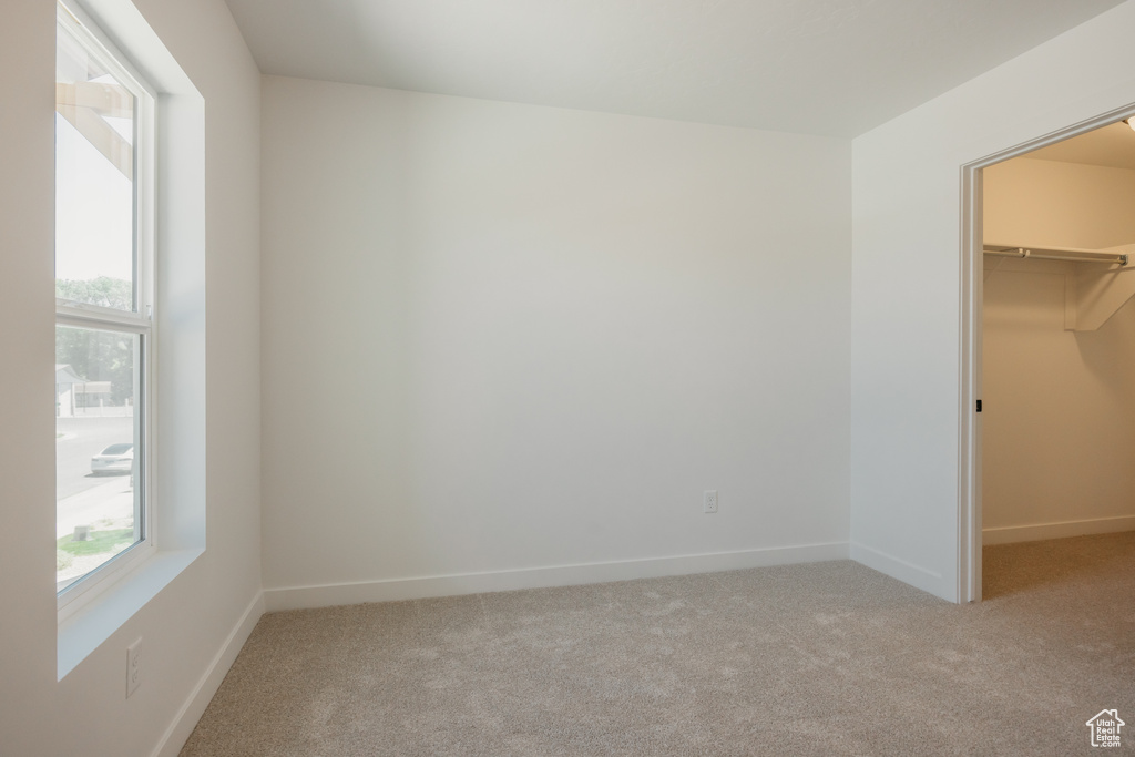 Unfurnished bedroom featuring a walk in closet, carpet, multiple windows, and a closet