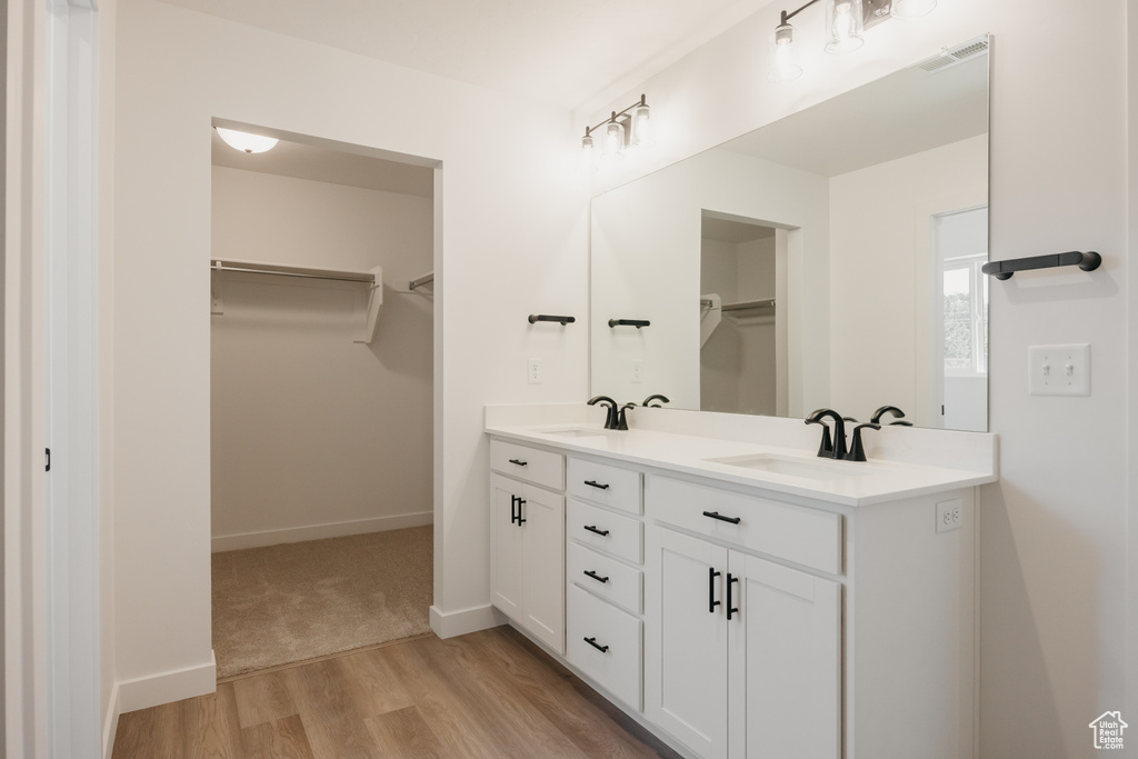 Full bath with double vanity, a walk in closet, and wood finished floors