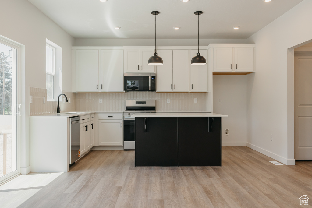 Kitchen with appliances with stainless steel finishes, light wood-type flooring, backsplash, a center island, and recessed lighting